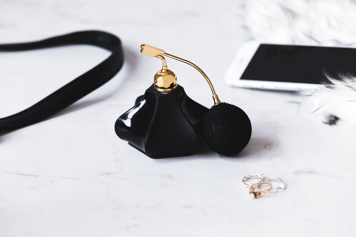 Flacon de parfum noir à poire dorée posé sur du marbre